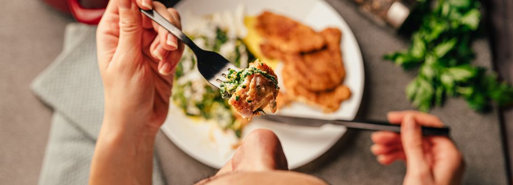 High angle shot looking down at woman eating low-carb meal, focus on lifting fork to mouth