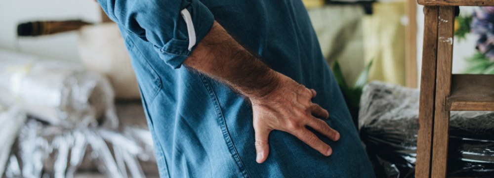 Older man hunched over and grabbing back with one hand 