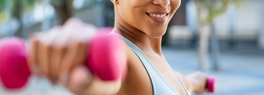 Woman strength training outdoors with pink dumbbell weights 