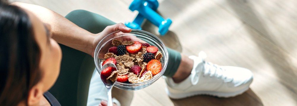 Woman sitting criss cross on floor after workout with bowl of granola in hand 